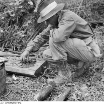 Australian soldier examines identity disc at the abandoned Sandakan Prisoner of War Camp. 